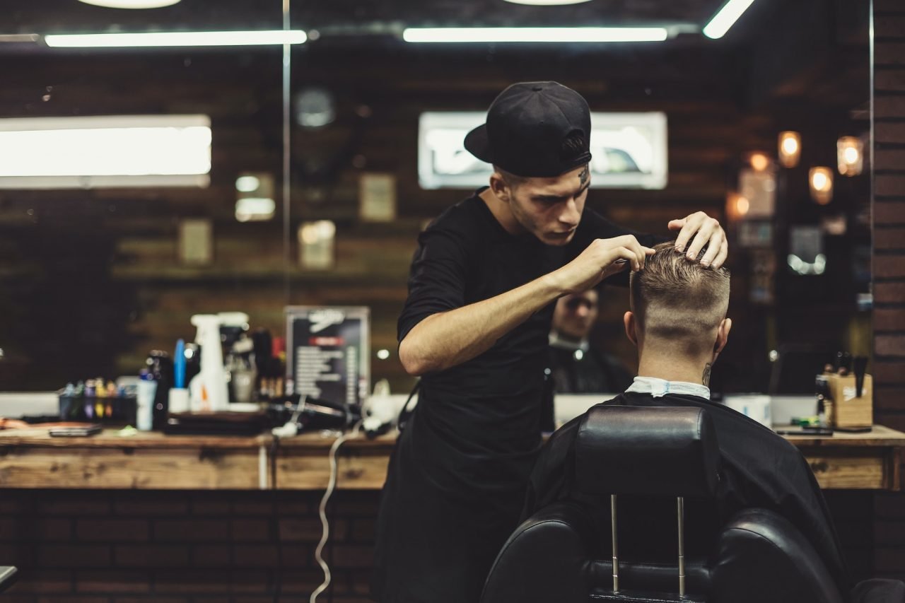 A barber styles a client's hair in a modern salon, surrounded by tools and mirrors, showcasing a professional grooming atmosphere.