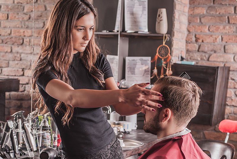 A hairstylist skillfully cuts a client's hair in a stylish barbershop, surrounded by tools and decorative elements.
